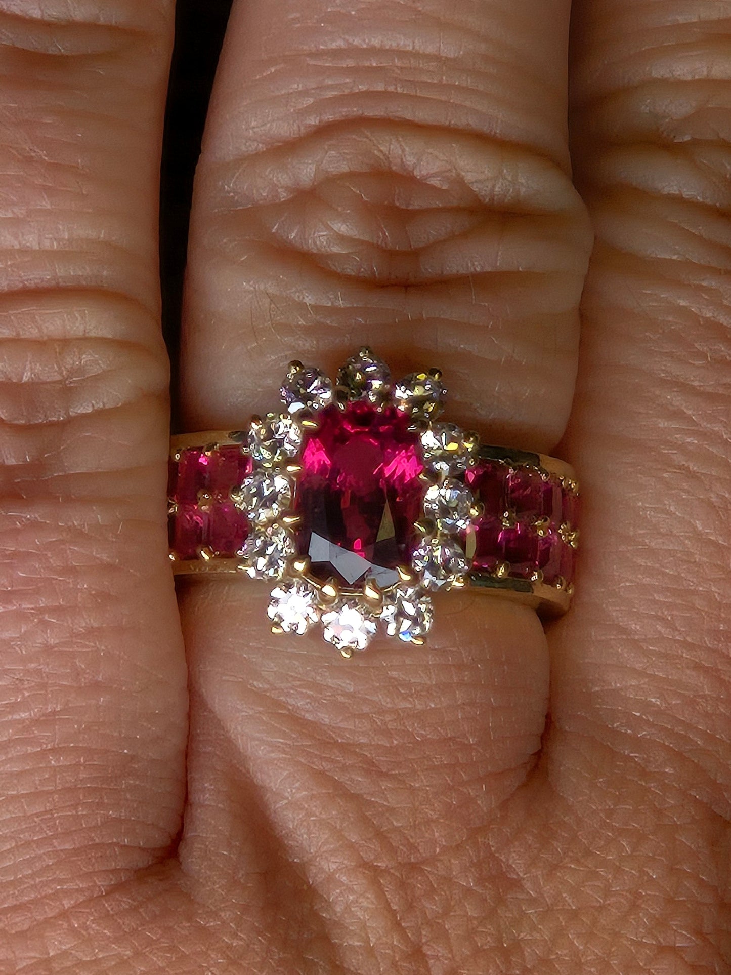 A close-up top view of the Crimson Bloom ring on a finger, highlighting the twelve old-European cut diamonds in the halo.