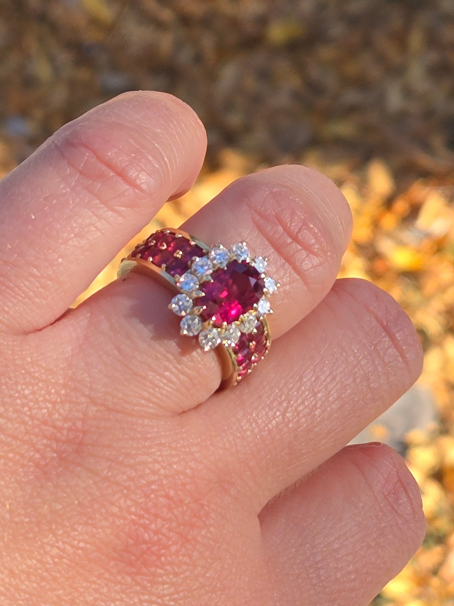 A close-up top view of the Crimson Bloom ring on a finger, highlighting the twelve old-European cut diamonds in the halo.