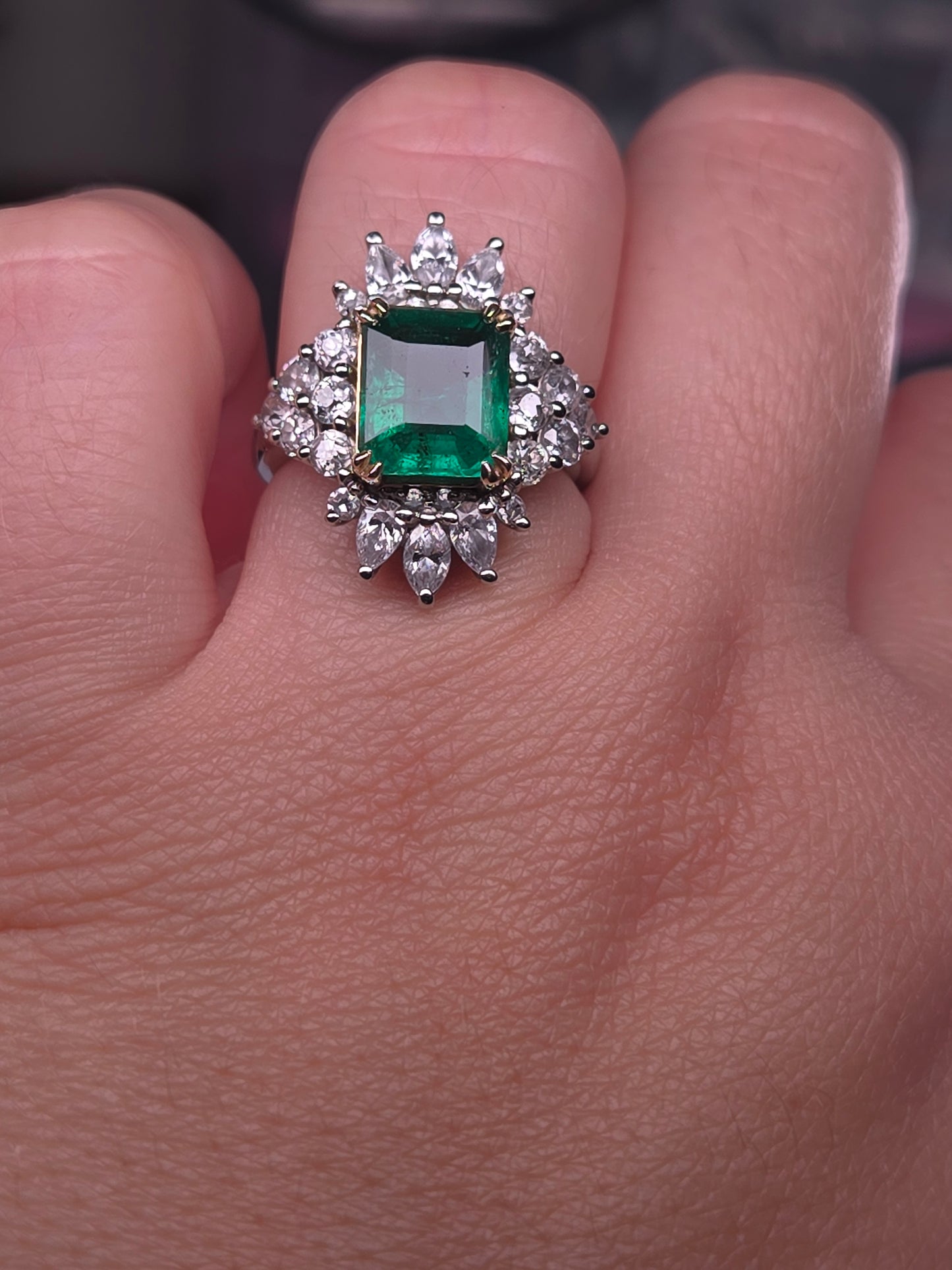 Angled view of the Emerald City Skyline emerald and diamond halo ring on a hand, showcasing its intricate details and sparkle.