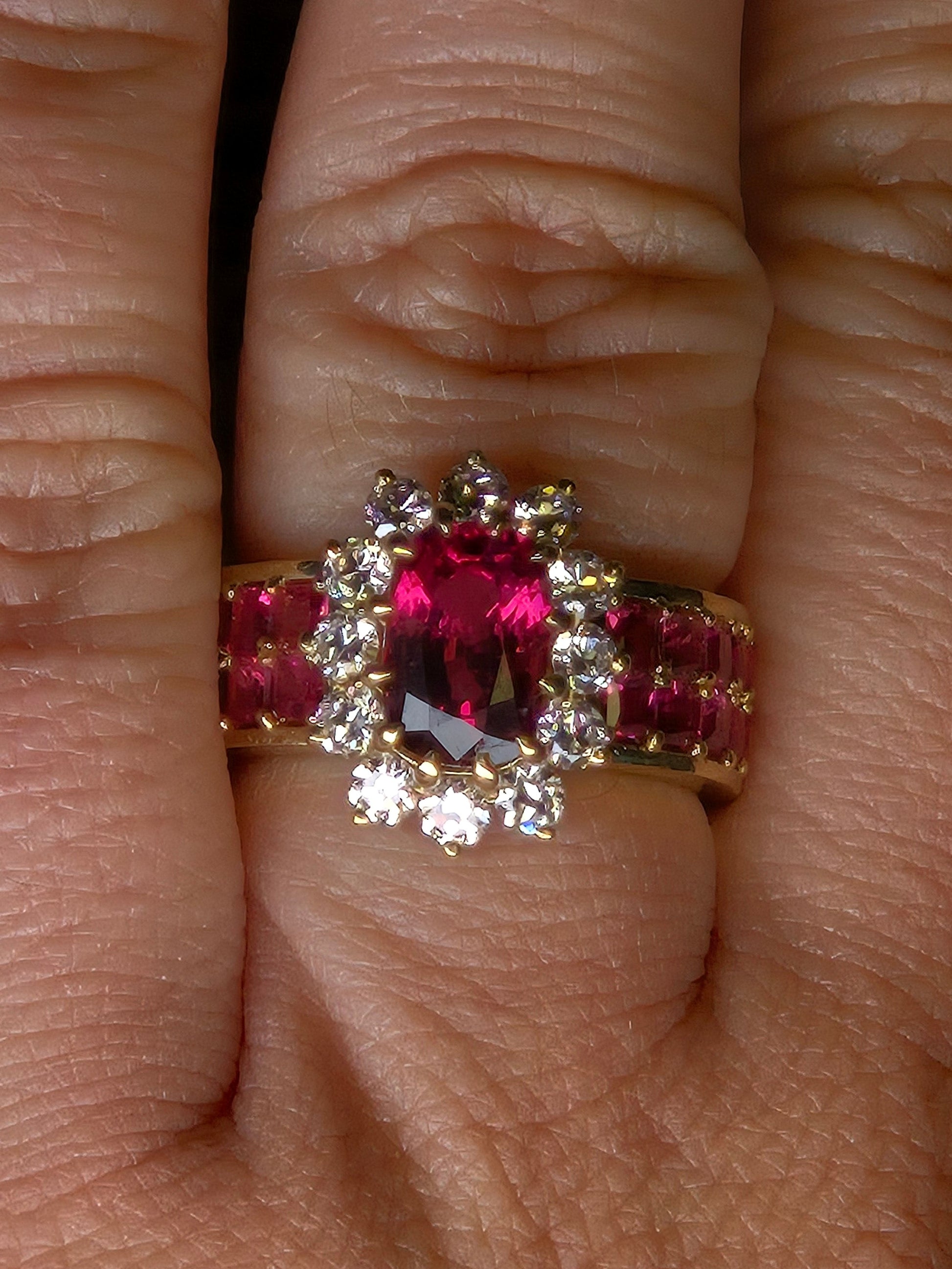 A close-up top view of the Crimson Bloom ring on a finger, highlighting the twelve old-European cut diamonds in the halo.